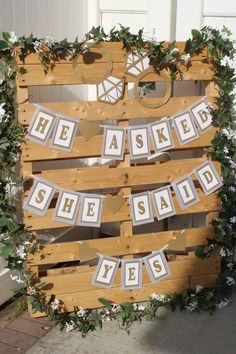 a wooden sign that says he asked she said yes with white flowers and greenery around it