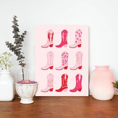 a pink poster with cowboy boots on it next to some vases and flowers in front of a white wall