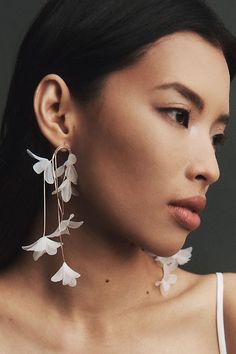 a woman wearing white earrings with flowers on it's sides and her face to the side