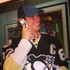 a woman talking on a cell phone while wearing a penguins jersey and cap with the number 22 on it