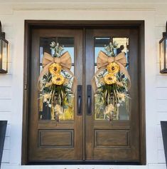 two wreaths on the front door of a house decorated with yellow flowers and greenery