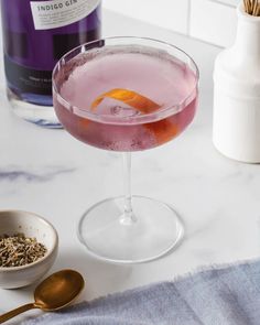 a pink cocktail with an orange peel garnish in the glass next to it