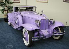 an old purple car is parked in a room with blue carpet and pictures on the wall