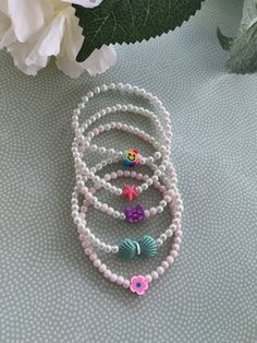 three bracelets with beads and flowers on a blue table next to a white flower