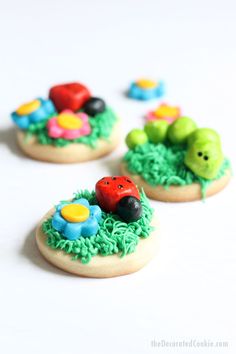 three decorated cookies sitting on top of a white table with green grass and ladybugs