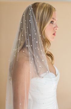 a woman in a wedding dress wearing a white veil with pearls on the top and bottom