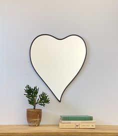 a heart shaped mirror sitting on top of a wooden shelf next to a potted plant