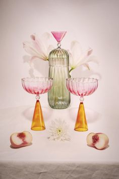 three glass vases with flowers and petals in front of a pink wallpapered background