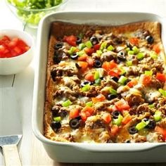 a casserole dish with meat and vegetables in it next to a bowl of tomatoes