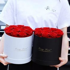 a person holding two boxes with red roses in them and the other one has a white shirt on