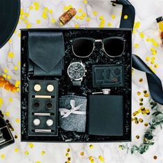 an assortment of men's accessories laid out on a marble counter top with yellow flowers in the background