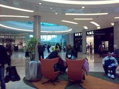 several people are sitting in chairs inside an airport lobby with large circular ceiling lights above them