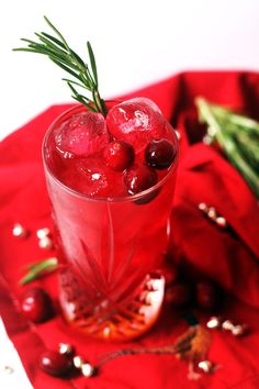 a drink with cherries and rosemary garnish in a glass on a red cloth