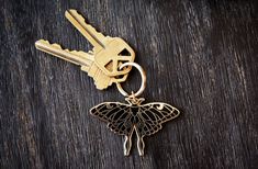 a butterfly shaped keychain sitting on top of a wooden table next to two keys