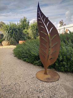 a metal sculpture with a large leaf on it's side in the middle of a gravel path