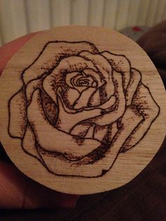 a hand holding a wooden stamp with a drawing of a rose on it's side