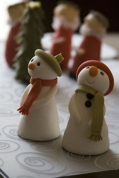 two snowmen with hats and scarves on top of a white table next to small christmas trees