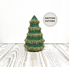 a green knitted christmas tree sitting on top of a wooden table next to a white wall