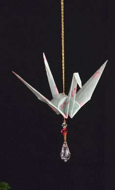 an origami bird hanging from a chain on a black background with a red bead