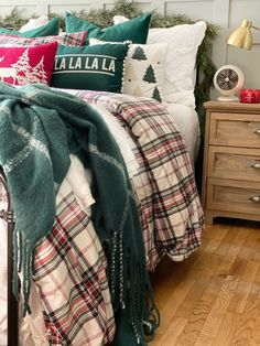 a bed with plaid blankets and pillows on top of it, next to a christmas tree