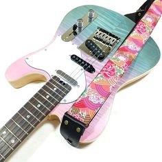 a pink and blue guitar strap with an intricate design on the neck, attached to a white electric guitar