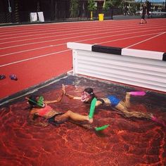 three women in bathing suits are laying on the ground near an empty track and one is holding a frisbee