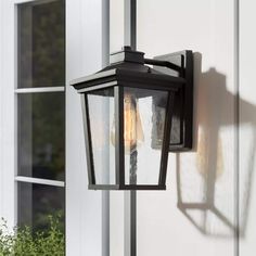 an outdoor light on the side of a white building next to a potted plant