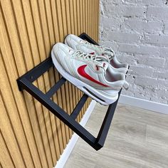 a pair of white and red sneakers are on a black shoe rack in front of a brick wall