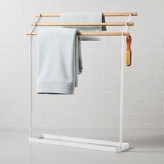 a white towel rack with two towels hanging on it and a wooden brush in the corner