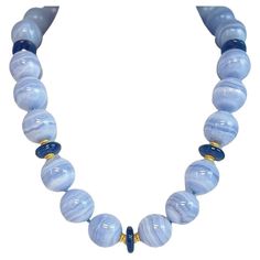 This eye-catching necklace features stunning blue lace agate and richly colored blue kyanite beads, hand strung with 18k yellow gold accents. The beautifully-matched agate beads are large, measuring 20mm in diameter, with the delicate blue striations that give this gemstone its lacy appearance, hence the elegant name! They have been paired with disc-shaped kyanite beads that have a beautiful royal, almost navy blue color. 18k yellow gold spacers and an 18k yellow gold hook-and-eye clasp give thi Luxury Hand-strung Round Beaded Necklaces, Blue Chalcedony Bead Necklaces, Blue Chalcedony Round Beads Necklace, Blue Agate Polished Bead Necklaces, Blue Chalcedony Gemstone Bead Necklaces, Blue Agate Beaded Necklace With Polished Beads, Blue Beaded Chalcedony Necklace, Blue Agate Polished Beads Necklace, Luxury Blue Gemstone Bead Necklaces