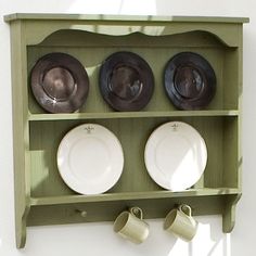 a green shelf with plates and cups hanging on it's side, against a white wall