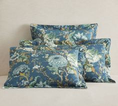 three pillows on a bed with blue and green floral print, one is made from linen