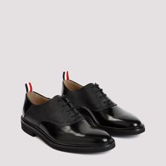 Thom Browne Black Leather Saddle Shoes. Pure black leather shoes, round toe, lace-up fastening on the top, textured leather effect details on the upper, tonal black rubber sole. Black, red and white stripes strap on the heels. Saddle Shoes, Pure Black, Mens Black Leather, Leather Cap, Black Leather Shoes, Red And White Stripes, Rubber Heels, Thom Browne, Black Rubber