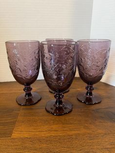 three purple glass goblets sitting on top of a wooden table next to a white wall