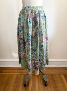 "Bright blue multicolored floral print midi-skirt, from the 1980s. Waist measures 14\" (36 cm) flat across and hip measures 22.5\" (57 cm) flat across. The skirt is 31\" (79 cm) long. The original size is a US 10. 100% polyester." Vintage Tiered Skirt Bottoms For Spring, Vintage Floral Print Tiered Skirt, Spring Vintage Gathered Skirt, Vintage Tiered Skirt With Floral Print, Vintage Green Tiered Skirt, Multicolor Floral Print Skirt For Garden Party, Vintage Full Skirt For Spring, 1970s Style Blue Bottoms For Spring, Vintage Relaxed Skirt For Spring