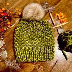 a green knitted hat sitting on top of a wooden table next to autumn decorations