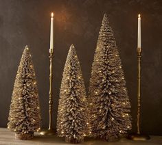 three gold christmas trees with lit candles in front of them on a wooden table next to a black wall