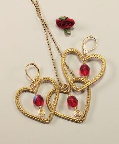 "This set of gold-toned heart earrings and necklace is embellished with sparkly red fire-polished crystal beads that flash blue and red when the light hits them. After shaping. they were woven with a fine non-tarnish gold-tone wire, and the bead dangles were added as a finishing touch.  The earrings have latch-back ear wires, and the ball necklace chain is 18\" long. Each piece is 1.25\" wide by 1 1.8\" tall. Will make a great Valentine's day gift for someone special, or just to show your love anytime of the year." Gold Plated Dangle Jewelry For Valentine's Day, Mother's Day Metal Jewelry With Matching Earrings, Handmade Festive Jewelry For Valentine's Day, Gold Heart Pendant Jewelry For Party, Heart-shaped Jewelry Set For Valentine's Day Party, Yellow Gold Metal Jewelry For Valentine's Day, Elegant Brass Jewelry For Valentine's Day, Handmade Jewelry For Valentine's Day Party, Valentine's Day Yellow Gold Metal Jewelry