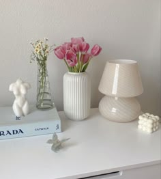 a white table with flowers and books on it, along with two small vases filled with pink roses