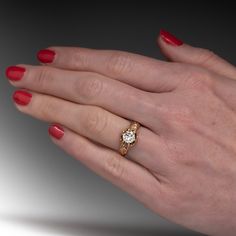 a woman's hand with red nail polish holding an engagement ring