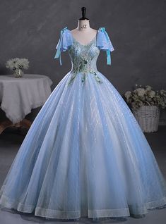 Amidst a sea of elegance, this Quinceanera dress stands out with its breathtaking beauty and charm. The delicate blue hue of the fabric creates a serene and magical aura, perfect for making a grand entrance. The bodice features intricate embroidery in green and silver, adding a touch of nature-inspired sophistication. Adorned with charming blue bows on the shoulders, the dress exudes a playful yet elegant vibe. The full skirt, crafted from layers of shimmering tulle, flows gracefully to the floor, creating a voluminous and ethereal silhouette. Sparkling details woven throughout the fabric catch the light beautifully, ensuring you shine with every movement. This dress is designed for those who wish to combine classic elegance with a modern twist, making it an ideal choice for a Quinceanera Princess Style Blue Evening Dress For Debutante Ball, Blue Tulle Quinceanera Dress For Banquet, Light Blue Tulle Gown For Quinceanera, Blue Princess Ball Gown With Sweetheart Neckline, Princess Blue Ball Gown With Sweetheart Neckline, Princess Style Blue Ball Gown With Sweetheart Neckline, Blue Princess Ball Gown With Fitted Bodice, Blue Tulle Ball Gown For Quinceanera, Blue Floor-length Wedding Dress For Quinceanera