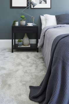 a bedroom with blue walls and carpeted flooring is pictured in this image, there are two framed pictures on the wall above the bed