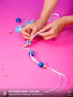 someone is making something out of candy on a pink surface with white string and blue beads