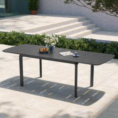 a black table sitting on top of a white tiled floor next to bushes and stairs