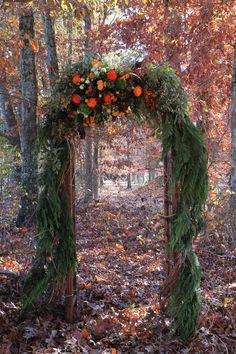 an arch made out of branches with flowers and greenery on it in the woods