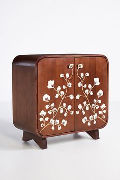 a wooden cabinet with white flowers painted on the front and side panels, sitting against a white background