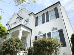 a white two story house with black shutters and red flowers on the front porch