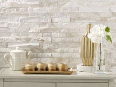 white flowers and vases sit on a table in front of a wall made of stone