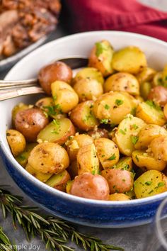 a bowl filled with potatoes and herbs on top of a table next to other dishes