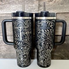 two black and silver travel mugs sitting next to each other on top of a table